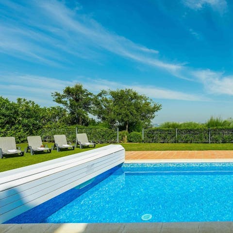 Laze on sun loungers by the pool surrounded by lush greenery