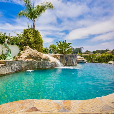 Swim in the pool with an elevated waterfall feature and slide