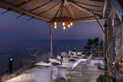 Dine alfresco under a thatched canopy as dusk falls over the sea