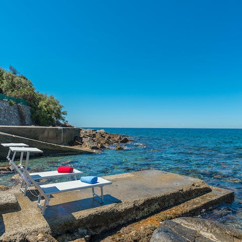Laze on loungers in the sun on the promontory before bathing in the turquoise Tuscan waters