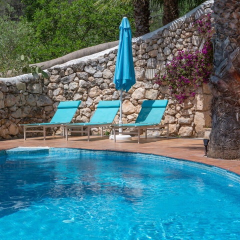 Lounge by the shared pool, surrounded by its warm stone wall